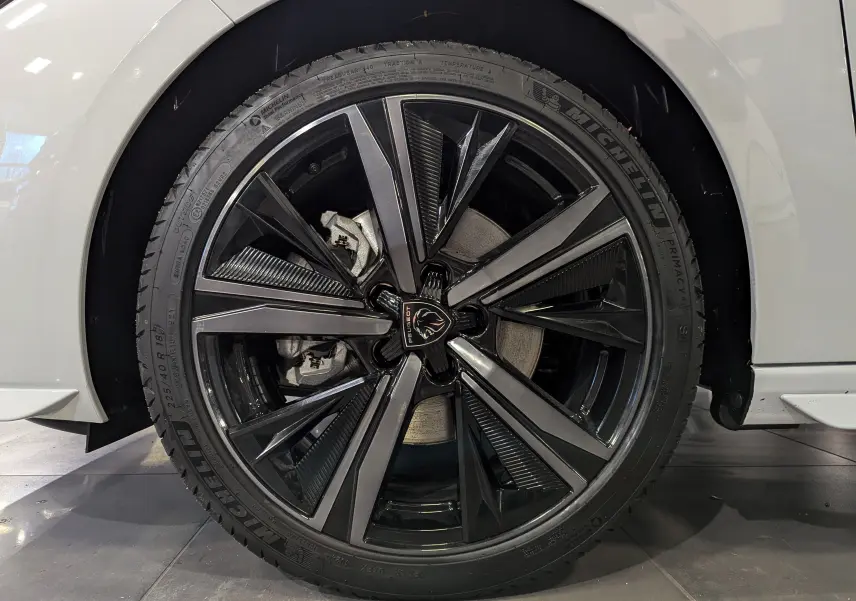 Gros plan sur la roue avant droite d'une Peugeot 308 GT blanche, avec jante alliage noire et grise au design moderne.