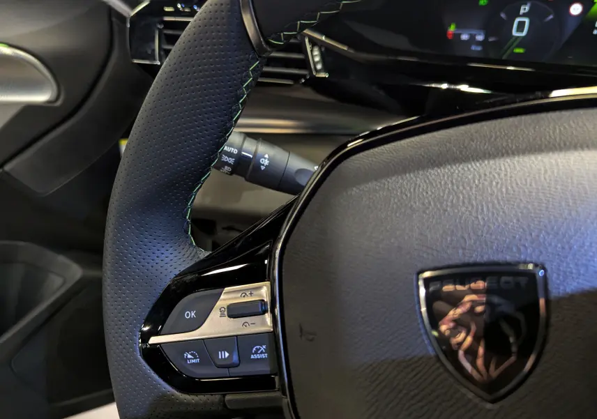 Gros plan sur le volant noir perforé de la Peugeot 308 2024 avec commandes intégrées et logo lion chromé.