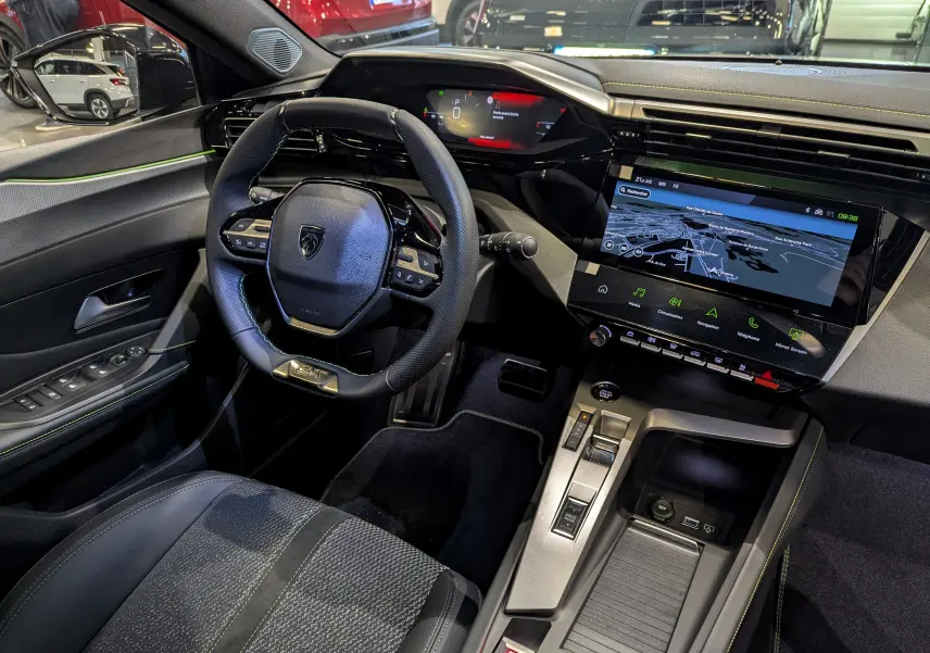 Vue intérieure côté conducteur de la Peugeot 308 GT 2024 avec volant compact, écran tactile et sellerie noire.