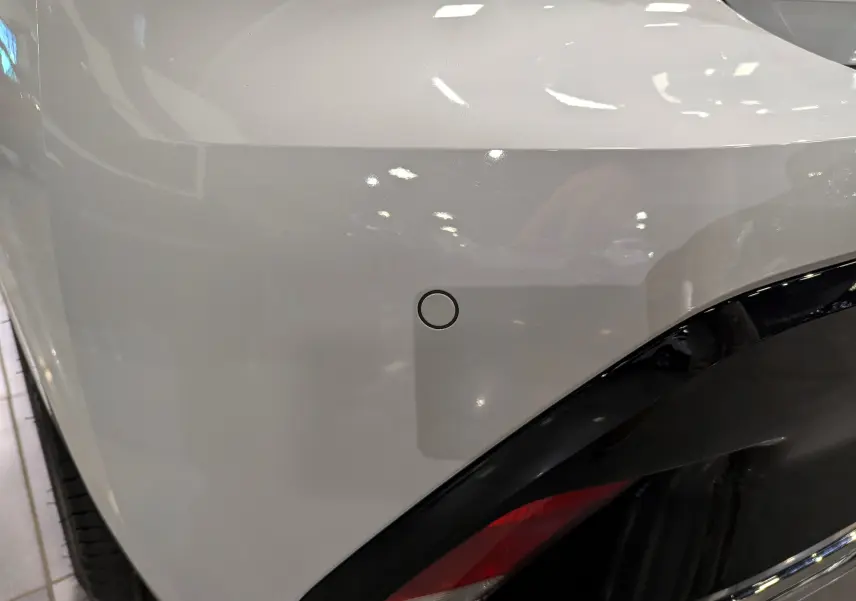 Détail du pare-chocs arrière blanc Okénite d'une Peugeot 308 2024 BlueHDi GT avec capteur de recul circulaire.