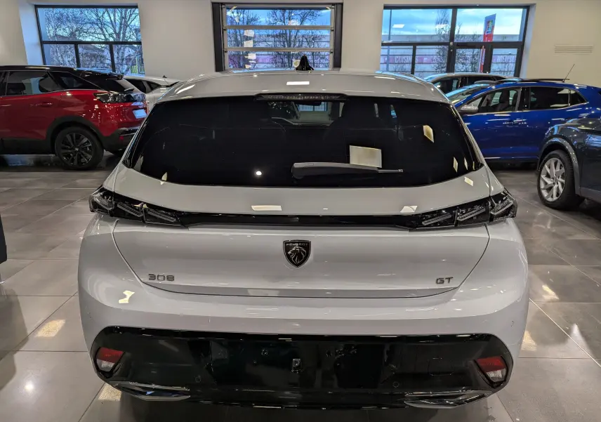 Vue arrière d'une Peugeot 308 GT blanche Okénite avec vitres teintées et feux arrière noirs en intérieur showroom.
