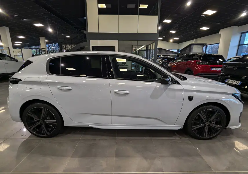 Profil côté gauche d'une Peugeot 308 GT blanche Okénite avec jantes noires et vitres teintées en showroom.