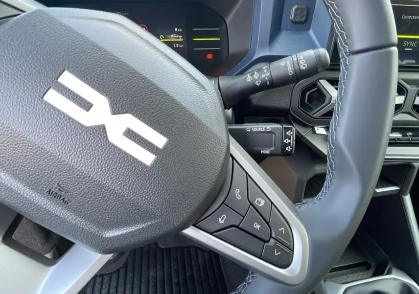 Gros plan sur le volant noir avec commandes intégrées du Dacia Bigster 2025, tableau de bord numérique en arrière-plan.