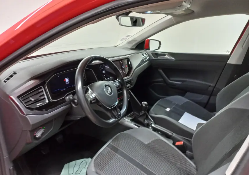 Vue intérieure côté conducteur d'une Volkswagen Polo Rouge Flash 2019 avec tableau de bord numérique et boîte manuelle.