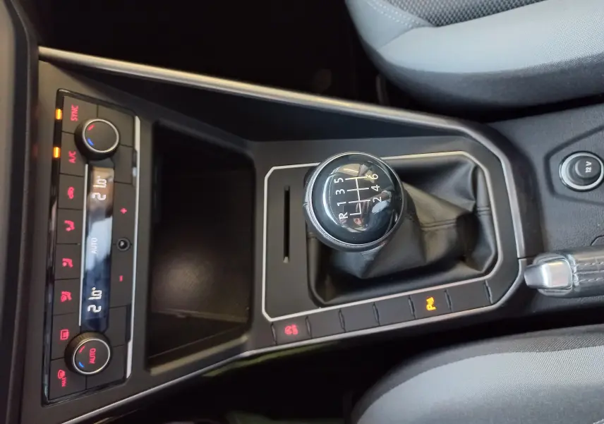 Vue rapprochée de la console centrale d'une Volkswagen Polo Rouge Flash 2019, mettant en valeur le levier de vitesses manuel et les commandes climatiques.