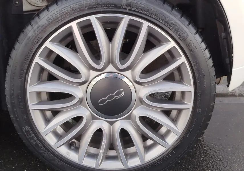 Vue rapprochée sur la roue avant gauche d'une Fiat 500 blanche Bossa Nova Pastel, montrant le passage de roue et le pneu.