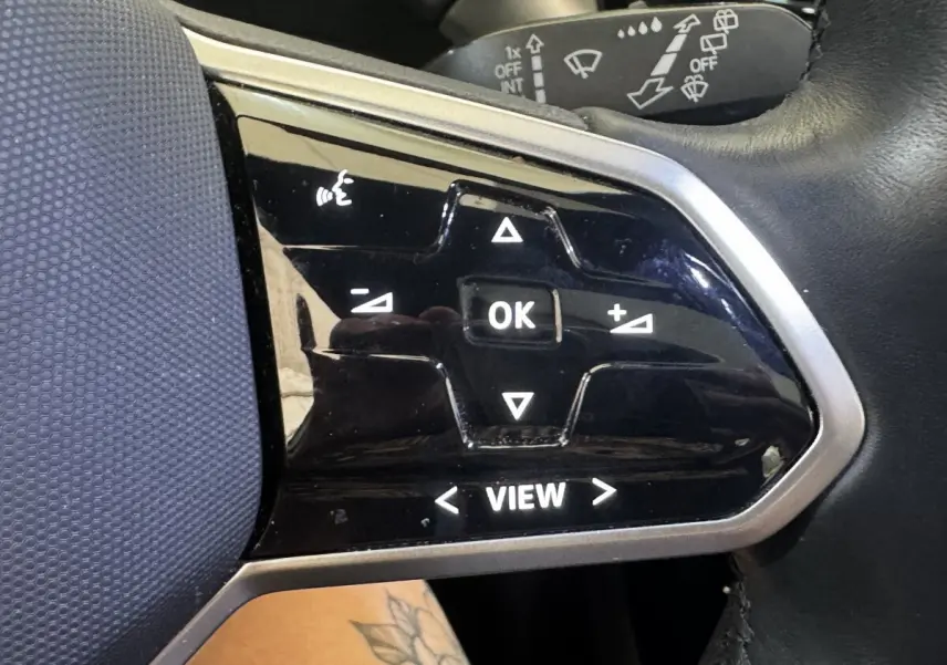 Gros plan sur les commandes noires du volant côté gauche du Volkswagen ID.4 blanc, avec boutons multifonctions éclairés.
