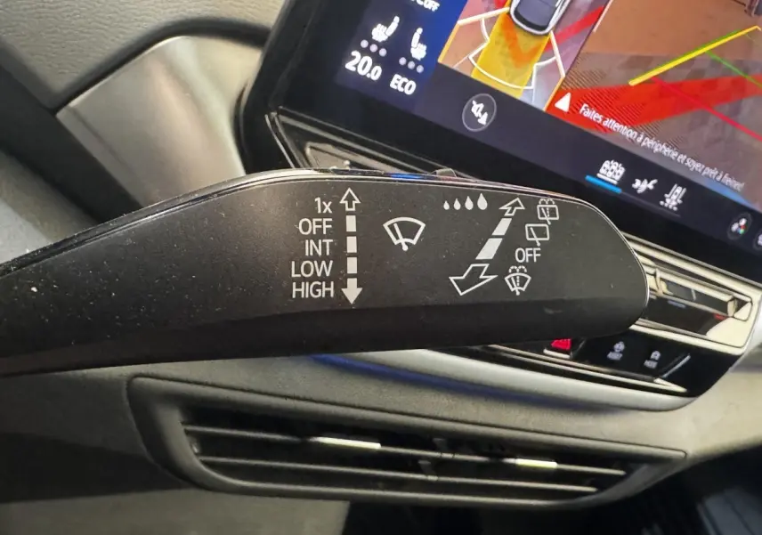 Gros plan sur la commande d’essuie-glace à gauche dans l’habitacle du Volkswagen ID.4 blanc, avec écran tactile en arrière-plan.