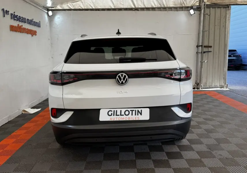 Vue arrière d’un Volkswagen ID.4 blanc avec feux arrière en bandeau et logo VW centré, stationné en intérieur.