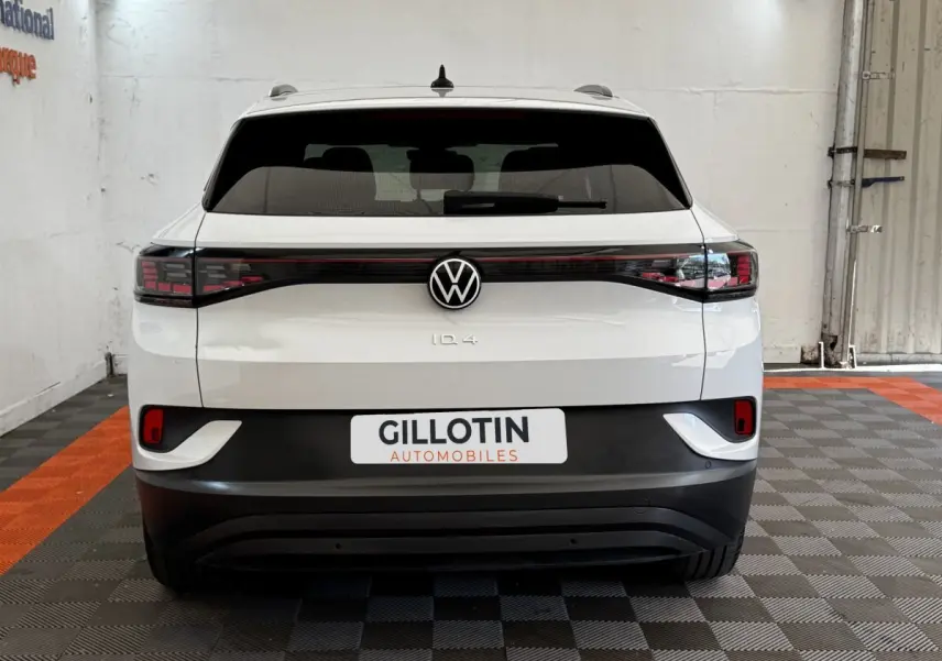 Vue arrière d'un Volkswagen ID.4 blanc avec feux arrière LED reliés et logo VW centré dans un garage.