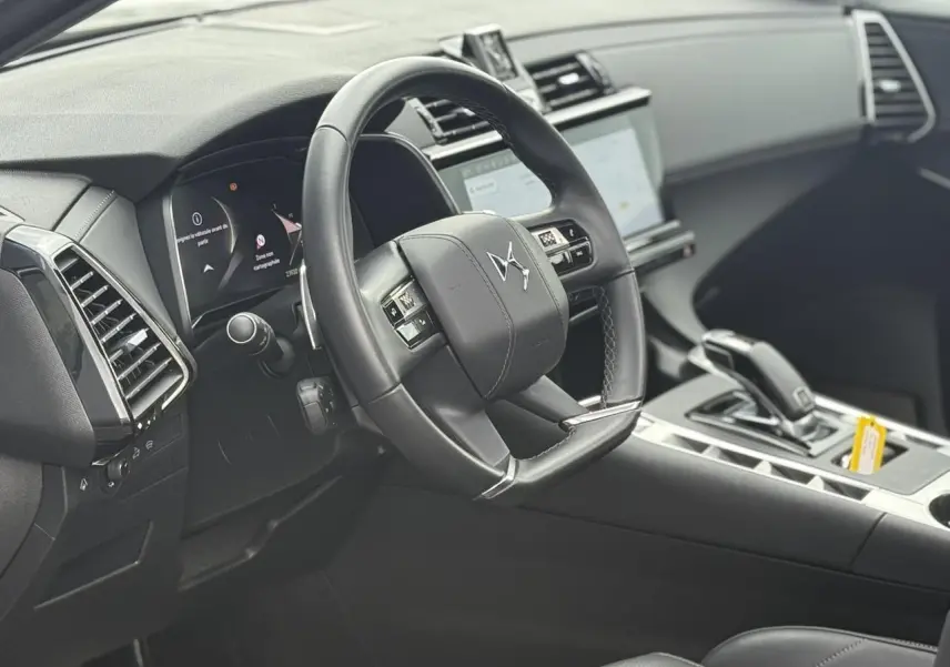 Intérieur noir du DS7 2025 vu côté conducteur, volant cuir avec commandes et écran tactile central visible.