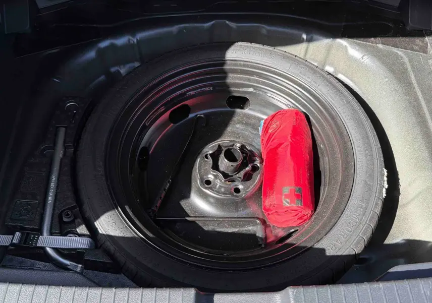 Gros plan sur la roue de secours noire du coffre d’un Volkswagen T-Roc 2025 avec trousse de secours rouge.