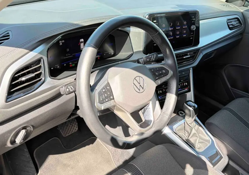 Vue intérieure du poste de conduite du Volkswagen T-Roc noir, avec volant cuir multifonctions et écran tactile central.