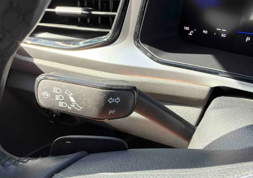 Gros plan sur la commande de clignotant et feux du Volkswagen T-Roc noir, intérieur côté gauche du volant.
