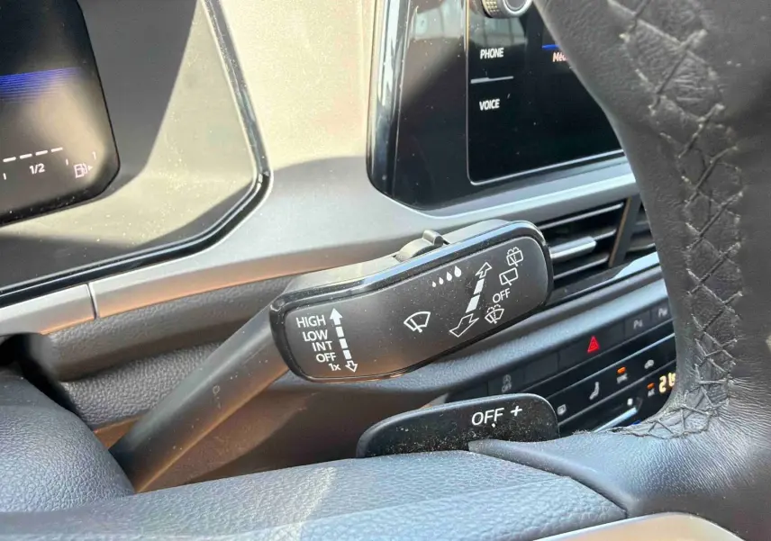 Gros plan sur le commodo d’essuie-glace et partie du volant cuir du Volkswagen T-Roc noir, tableau de bord digital en arrière-plan.