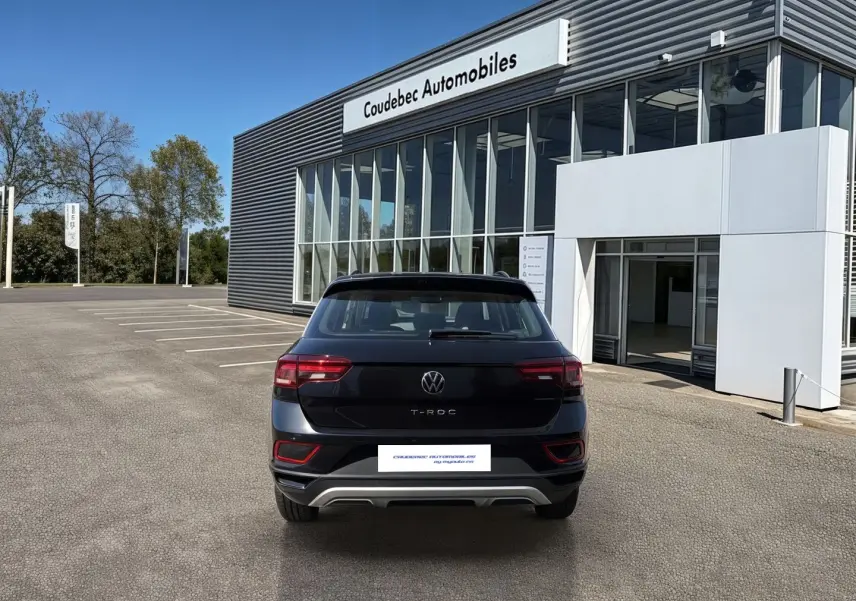 Vue arrière d'un Volkswagen T-Roc noir stationné devant un bâtiment moderne de concession automobile.