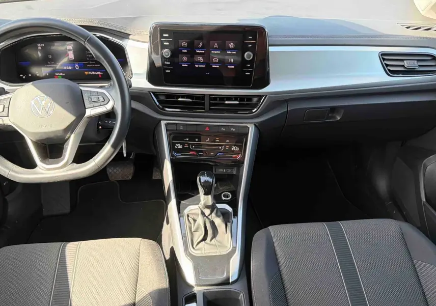 Vue intérieure avant du Volkswagen T-Roc 2025 avec tableau de bord moderne, écran tactile et levier de vitesse manuel.