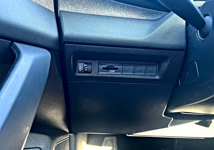 Détail du tableau de bord côté gauche en plastique noir avec commande de réglage des phares sur Peugeot 308 2025.
