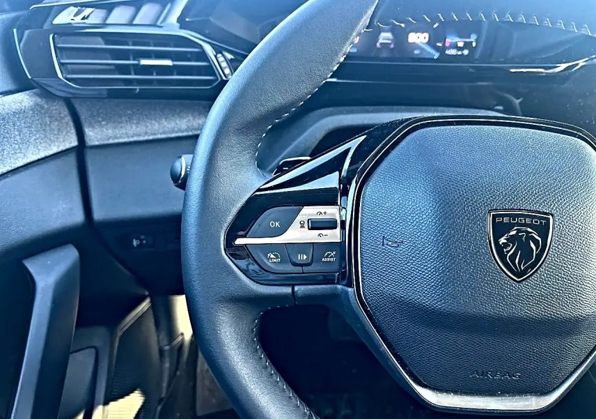 Vue rapprochée du volant multifonction noir de la Peugeot 308 gris selenium, avec tableau de bord numérique en arrière-plan.