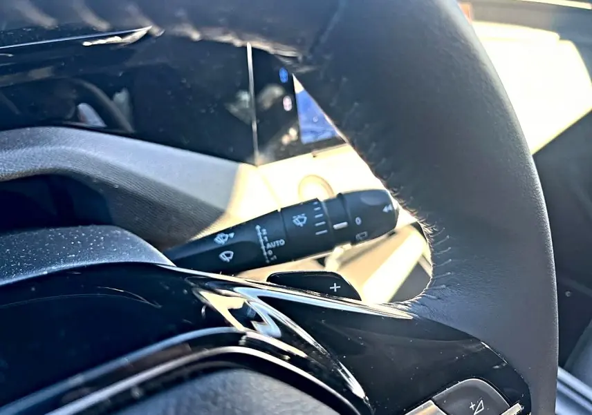 Gros plan sur le volant noir de la Peugeot 308 gris selenium, avec commandes multifonctions et palettes au volant visibles.