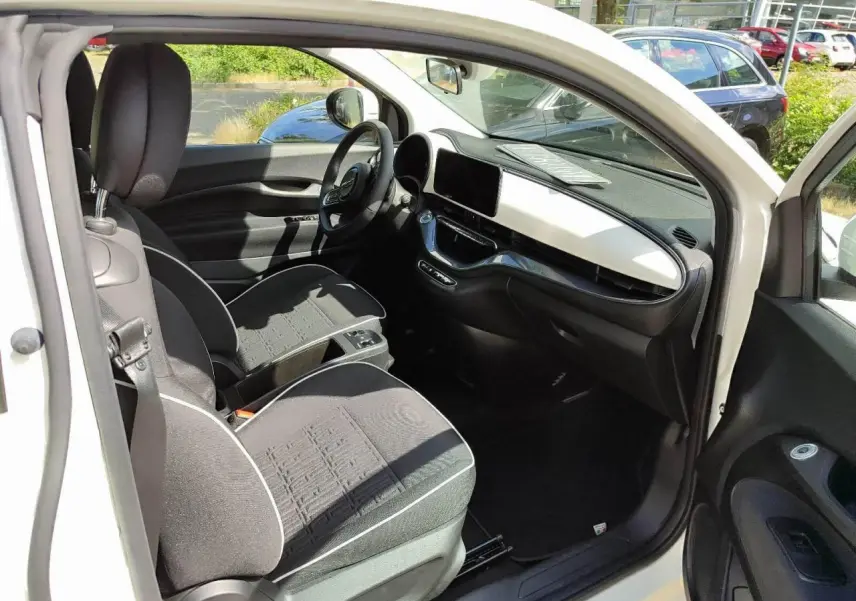 Intérieur de la Fiat 500 électrique 2024 vue côté conducteur, sièges noirs avec surpiqûres blanches et tableau de bord blanc.