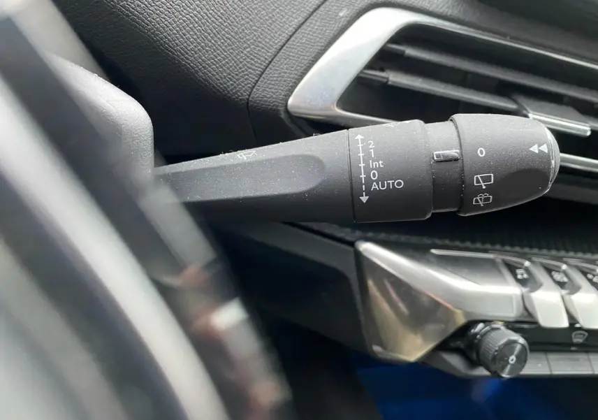 Gros plan sur la commande des essuie-glaces à gauche du volant dans l'habitacle noir du Peugeot 3008 gris platinium.