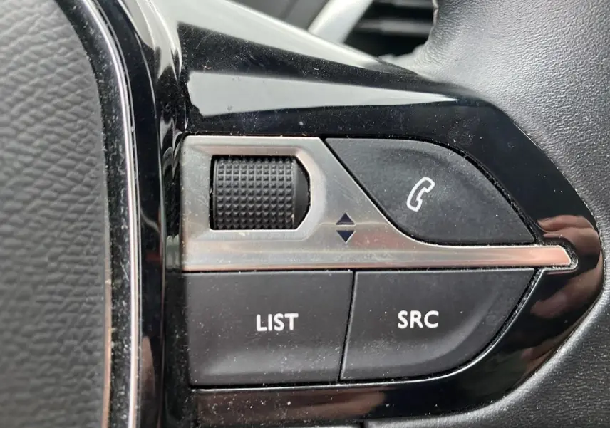 Gros plan sur les commandes du volant noir du Peugeot 3008 gris platinium, boutons pour téléphone et liste audio.