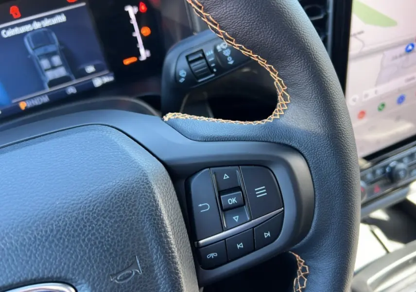 Gros plan sur le volant en cuir noir avec surpiqûres orange du Ford Ranger 2025 gris carbone, montrant les commandes intégrées.