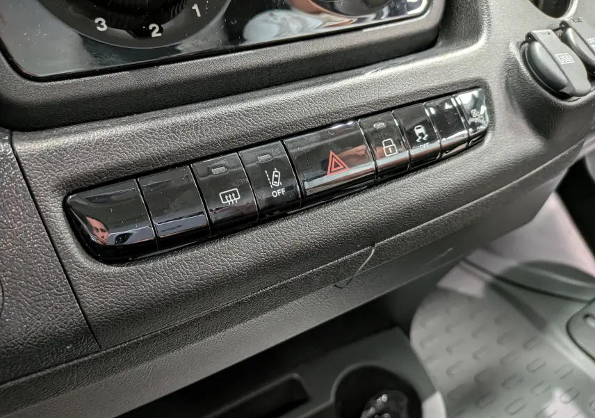 Gros plan sur la rangée de boutons noirs du tableau de bord du Fiat Ducato Fourgon blanc, avec commandes de sécurité et verrouillage.