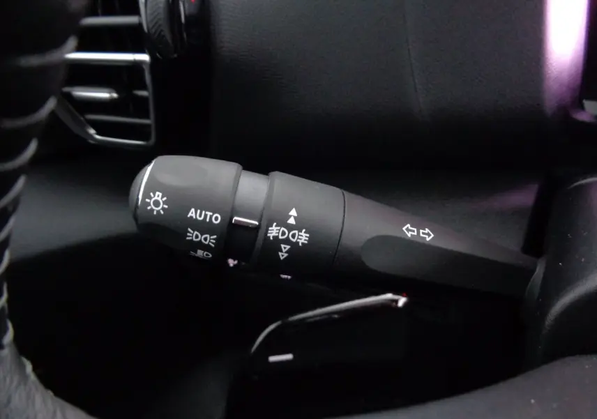 Gros plan sur la commande des phares et clignotants à gauche du volant dans l’habitacle noir du Citroën C4 gris 2023.