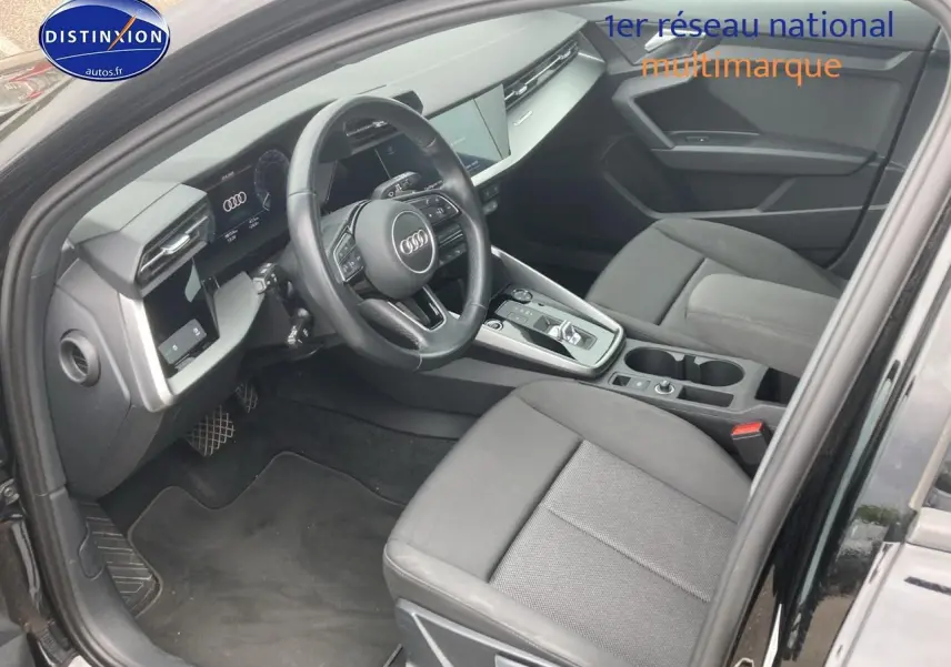 Vue intérieure côté conducteur de l'Audi A3 Sportback noire, mettant en valeur le volant cuir multifonction et la console centrale moderne.