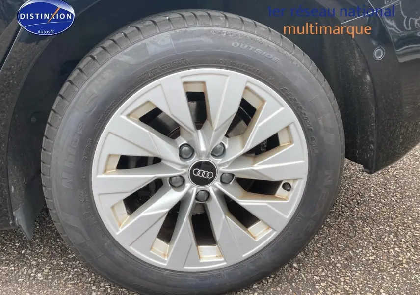 Gros plan sur la jante alu argentée avec logo Audi d'une Audi A3 Sportback noire, côté avant droit.