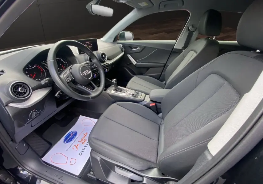 Vue intérieure côté conducteur de l'Audi Q2 35 TFSI S-Line 2023 avec sièges tissu noir et tableau de bord moderne.