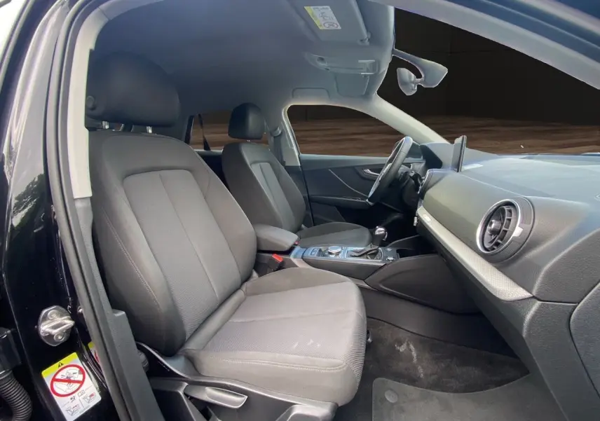 Intérieur noir de l'Audi Q2 2023 vu côté conducteur, avec sièges tissu et tableau de bord moderne.