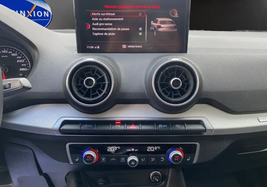 Tableau de bord de l'Audi Q2 35 TFSI 2023 avec écran central affichant les aides à la conduite et commandes climatisation.