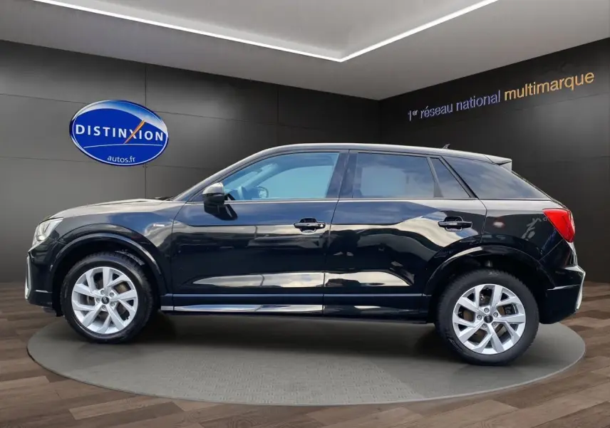 Audi Q2 noir mito vue de profil côté gauche, avec jantes alliage 17 pouces et hayon motorisé visible en arrière-plan.
