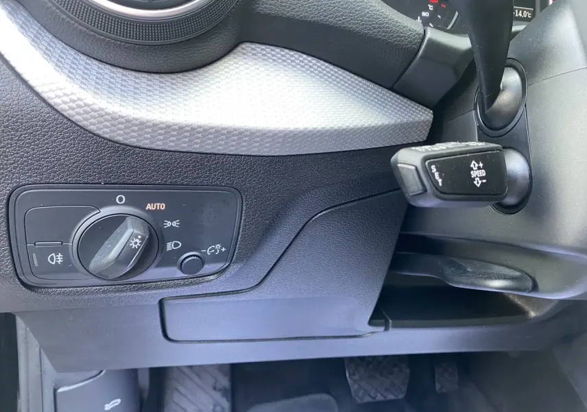 Détail du tableau de bord noir de l'Audi Q2 2023 montrant la commande des phares et le levier de régulateur de vitesse.