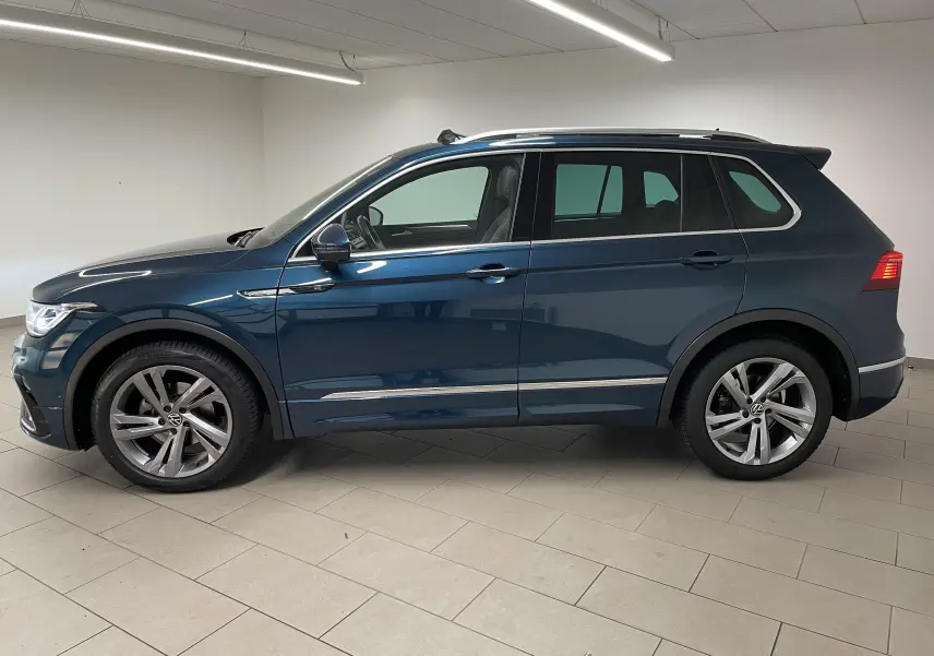 Volkswagen Tiguan 2024 bleu Nightshade en profil droit, avec jantes alliage et attelage escamotable visible à l'arrière.