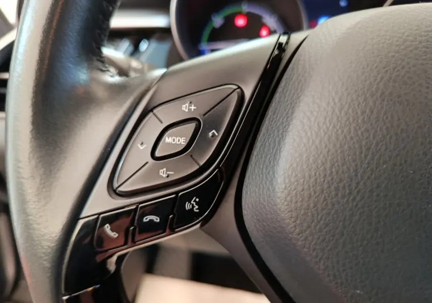 Gros plan sur les commandes gauche du volant cuir noir du Toyota C-HR gris clair, avec boutons mode et appels.