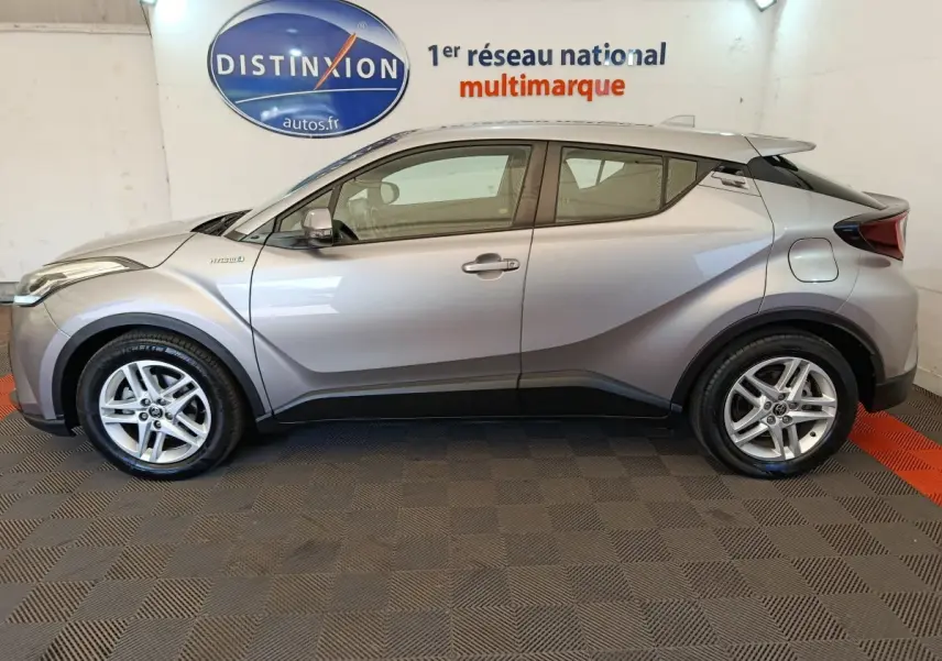 Profil côté gauche d'un Toyota C-HR gris clair hybride 2022, avec jantes alliage et lignes anguleuses distinctives.