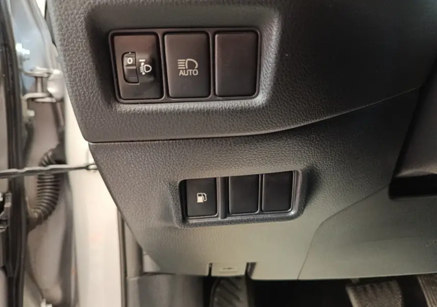 Gros plan sur les commandes côté gauche du tableau de bord du Toyota C-HR gris clair, avec interrupteurs phares et ouverture réservoir.