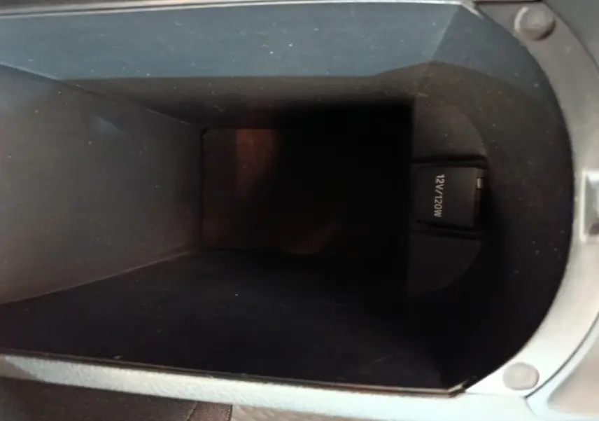 Vue intérieure du compartiment de rangement central noir avec prise 12V visible dans un Toyota C-HR gris clair.
