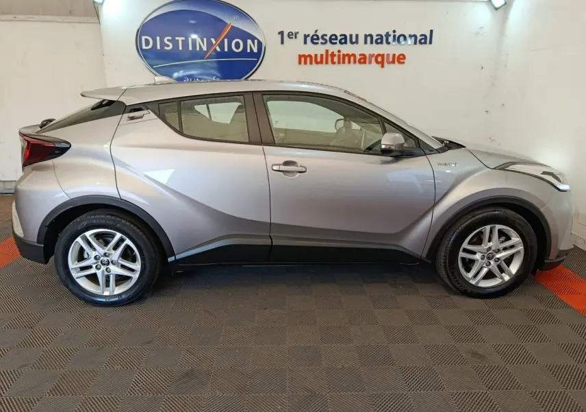 Vue latérale droite d'un Toyota C-HR gris clair 2.0 Hybride 184 Dynamic Business Beyond, en intérieur showroom.