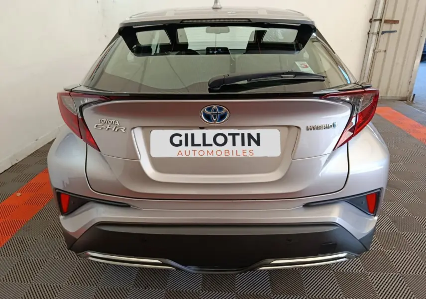 Vue arrière d'un Toyota C-HR gris clair hybride 2022 avec feux arrière anguleux et logo Toyota visible.