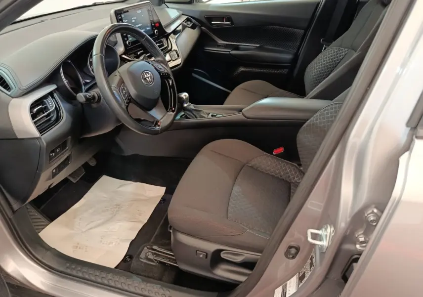 Intérieur côté conducteur du Toyota C-HR gris clair 2022, avec tableau de bord moderne et sièges tissu noirs.