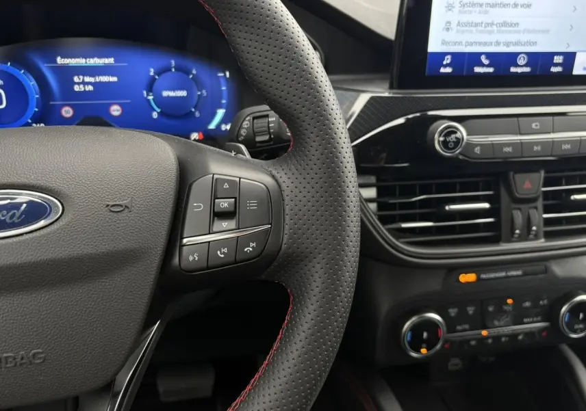 Vue rapprochée du volant perforé noir avec surpiqûres rouges et tableau de bord numérique du Ford Kuga 2023.