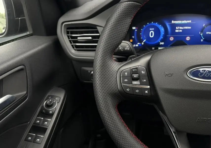 Vue rapprochée du volant perforé noir avec surpiqûres rouges et tableau de bord numérique du Ford Kuga 2023.
