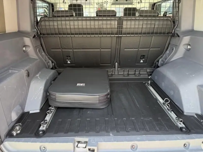 Vue intérieure du coffre de l'INEOS Grenadier beige 2024, avec séparation grillagée et sac de rangement noir posé.