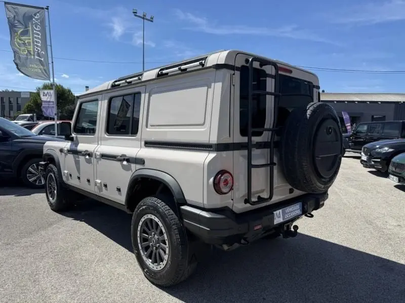 Vue 3/4 arrière droite d’un INEOS GRENADIER beige 2024 avec roue de secours et échelle sur porte arrière.