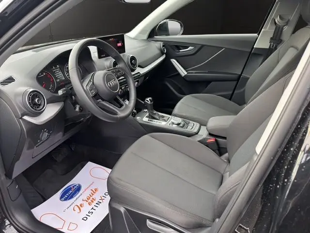 Intérieur noir de l'Audi Q2 35 TFSI 2023 vu côté conducteur, avec tableau de bord digital et sellerie tissu.